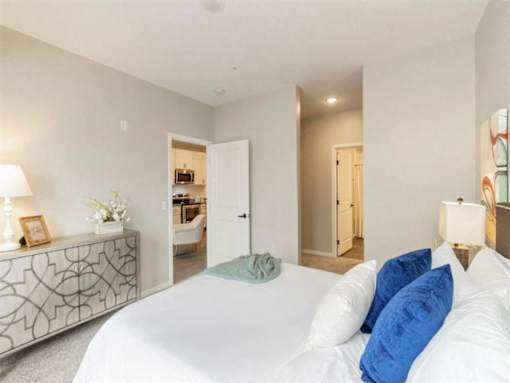 A bedroom with a large bed and a dresser with a lamp on it at The Barnum Apartments, White Bear Lake