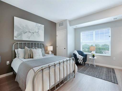 A bedroom with a large bed and a chair by the window at The Barnum Apartments, White Bear Lake, Minnesota