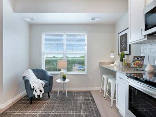A kitchen with a grey chair and a table with a white cloth on it at The Barnum Apartments, White Bear Lake, MN,  55110