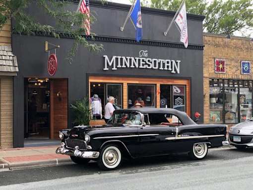 A black vintage car is parked in front of a building with a sign that says at The Barnum Apartments, White Bear Lake
