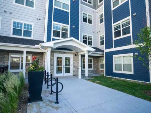 A building with a white and blue exterior and a covered walkway entrance at The Barnum Apartments, White Bear Lake, MN,  55110