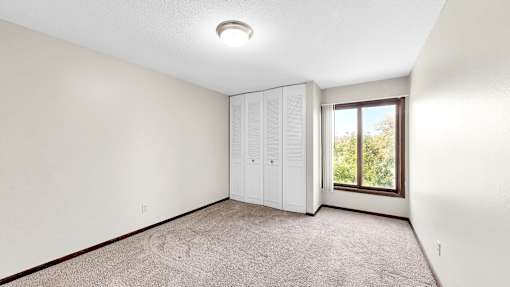 A room with a carpeted floor and a window showing greenery outside.
