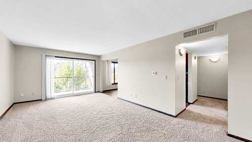 A spacious room with a carpeted floor and a sliding glass door leading to a balcony.