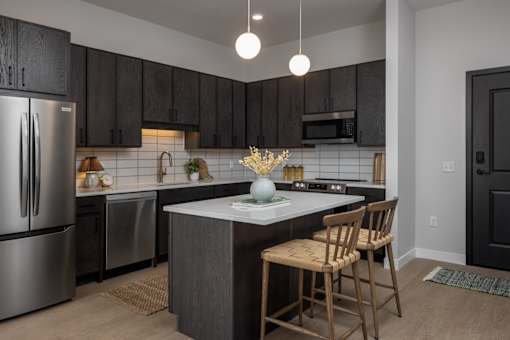 A kitchen with a refrigerator, sink, and bar stools.