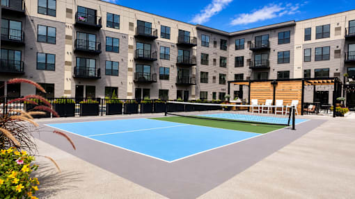 A tennis court is located in front of a large apartment building.