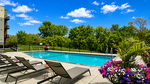 A pool surrounded by lounge chairs and trees.