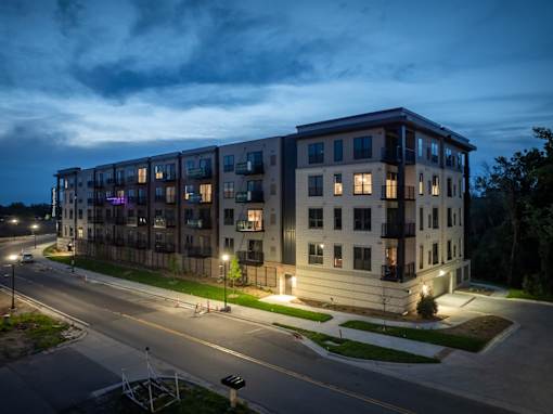 A modern apartment building is lit up at dusk with street lights on.