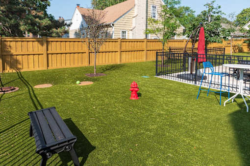 A backyard with a black bench and a red fire hydrant.