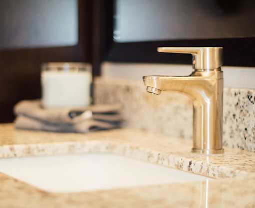 A bathroom sink with a marble countertop and a gold faucet.