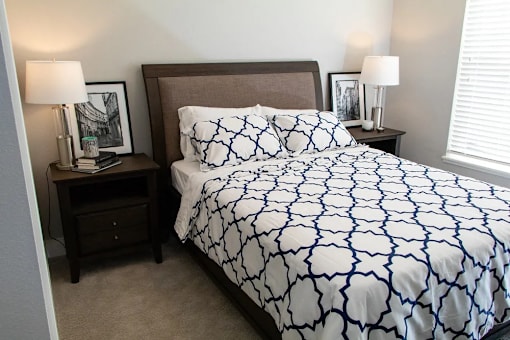 A bed with a white and blue patterned comforter sits in a room with two lamps on either side.