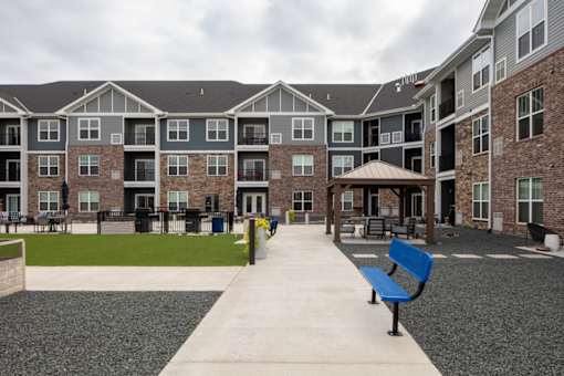A long concrete walkway leads to a building with a blue bench on the right side.
