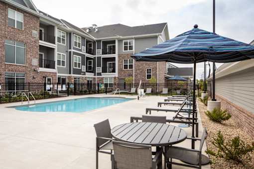 A pool area with a table and chairs and umbrella in front of apartment buildings.