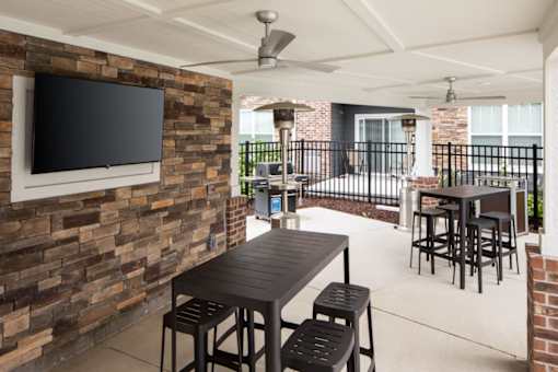 A patio with a table and chairs and a television on a brick wall.
