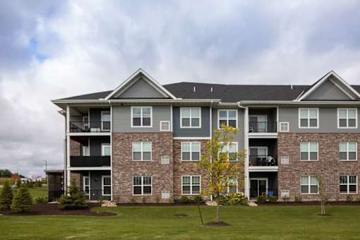 A large apartment building with a grassy front yard and a yellow tree.