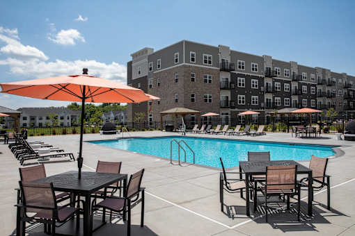 A pool area with chairs and umbrellas in front of a building at The Edison at Woodbury, Woodbury, 55129