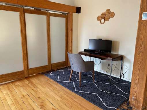 A room with a wooden floor, a chair, a table with a TV on it, and a rug.