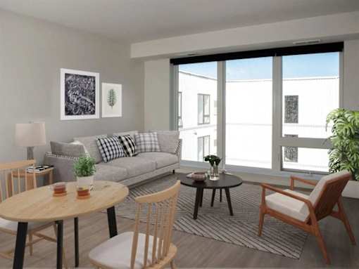 A living room with a grey couch, a wooden table, and a chair at The Redwell Apartments, Minneapolis, Minnesota