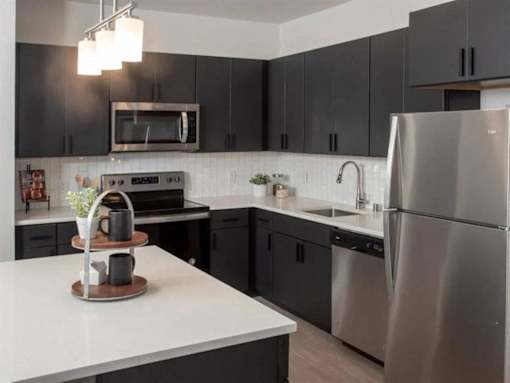A modern kitchen with a stainless steel refrigerator and black cabinets at The Redwell Apartments, Minneapolis