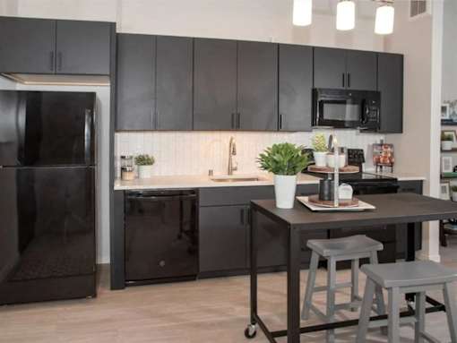A black fridge and microwave in a kitchen with a table and stools at The Redwell Apartments, Minneapolis, Minnesota