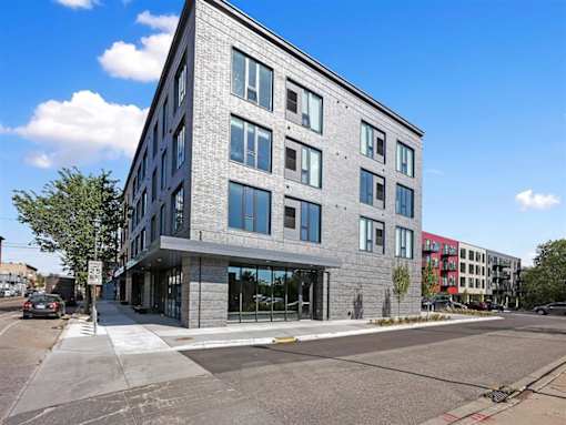 A modern building with a grey facade and large windows is situated on a street corner.