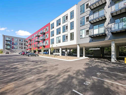 A parking lot in front of a multi-story building with cars parked.