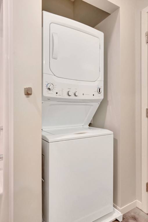 A white dryer and washer are stacked in a small, white-walled laundry room at Soul Apartments, St. Paul