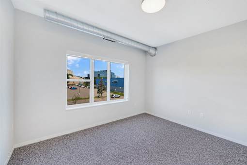 A room with a window showing a view of a parking lot and trees at Soul Apartments, St. Paul, 55107