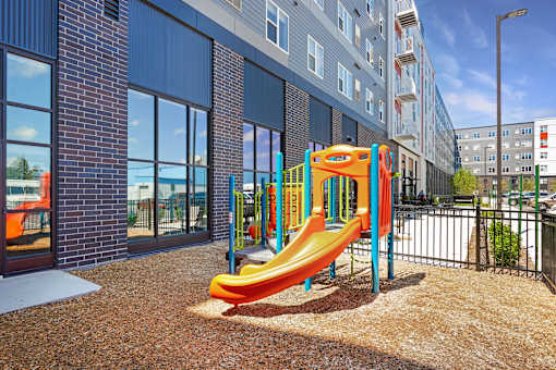 A playground with a yellow slide in front of a building at Soul Apartments, St. Paul