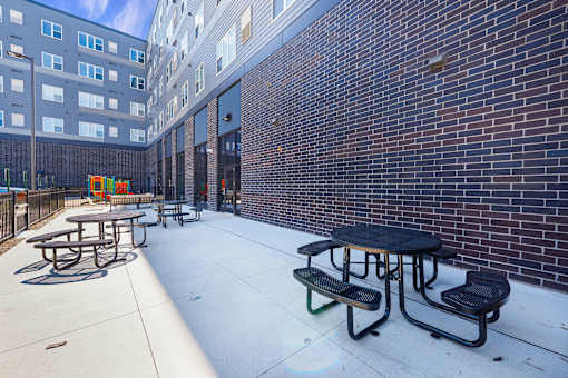 A patio with tables and benches is surrounded by a brick wall at Soul Apartments, Minnesota