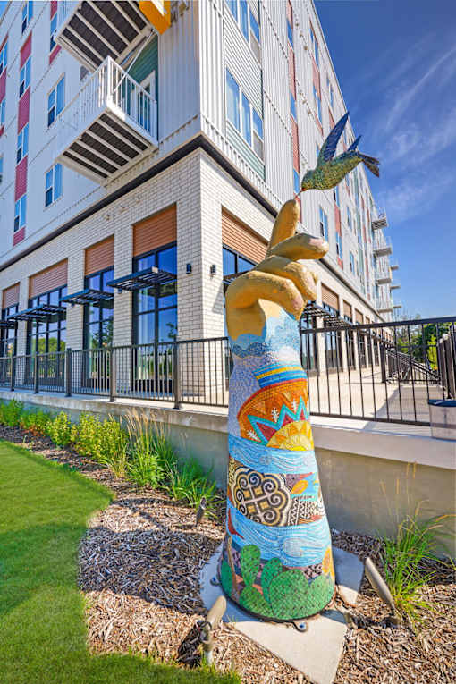 A colorful sculpture of a bird is in front of a building at Soul Apartments, St. Paul