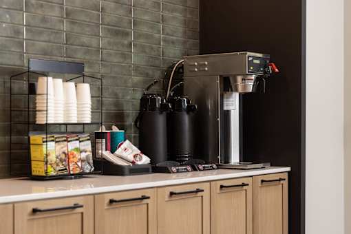 A coffee machine is on a counter with a stack of paper cups to its left.