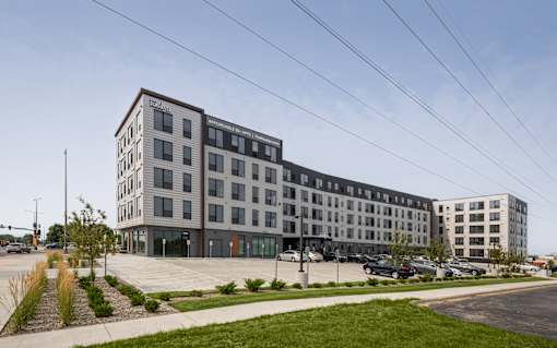 A modern multi-story building with a parking lot in front.