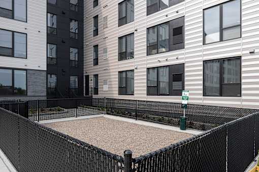 A black fenced sandbox in front of apartment buildings.