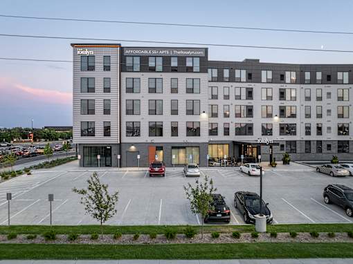 A parking lot in front of a multi-story building with a sign that says "Affordable US Apartments".