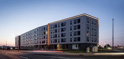 A modern multi-story building with a flat roof and a mix of windows and balconies.