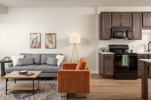 A living room with a grey couch, a coffee table, and a kitchen area in the background.