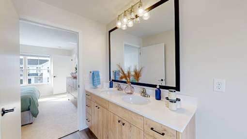 A bathroom with a vanity, mirror, and a bedroom in the background.