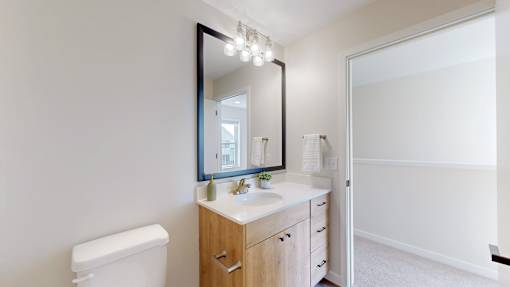 A bathroom with a toilet, sink, mirror, and lights.