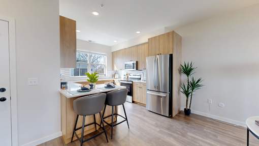 A kitchen with a refrigerator, bar stools, and a dining table.