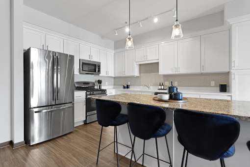 A kitchen with a refrigerator, microwave, oven, and bar stools.