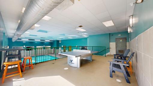 A room with a ping pong table and chairs.