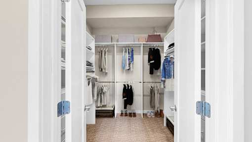 A white walk in closet with clothes hanging on shelves.