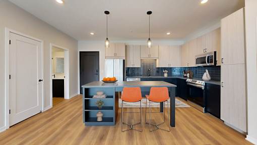 A kitchen with a blue island and orange chairs.