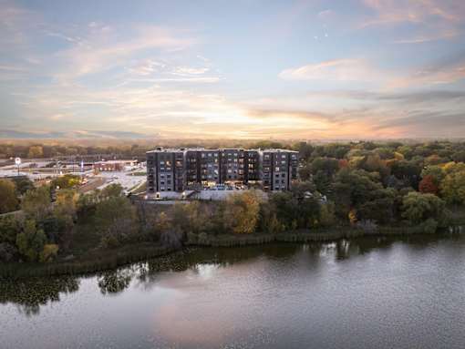 A modern building is situated by a body of water with trees in the background.
