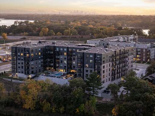 A large apartment complex is surrounded by trees and is lit up at dusk.