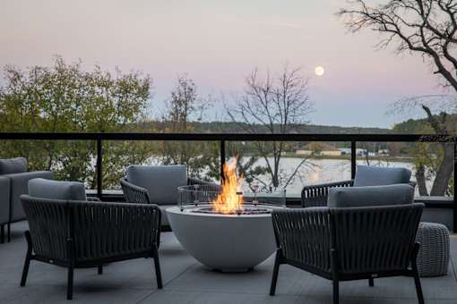 A fire pit sits in the middle of a patio surrounded by chairs.