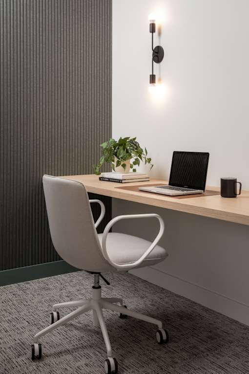 A modern office chair is placed in front of a wooden desk with a laptop, a plant, and a black mug on it.