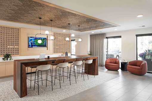 A modern office space with a long wooden table and chairs, a television on the wall, and a view of the city outside the windows.