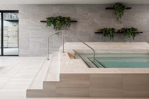 A modern indoor swimming pool with a glass enclosure and a wooden ledge.
