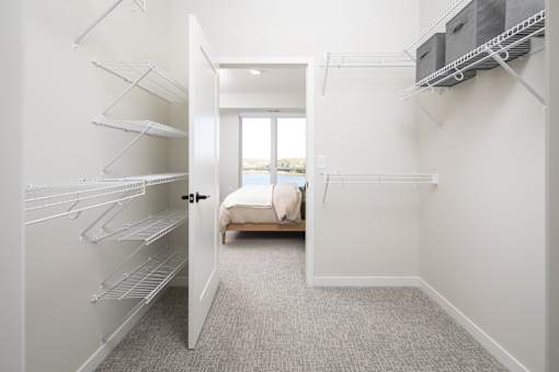 A white walk-in closet with shelves and a doorway leading to a living room.
